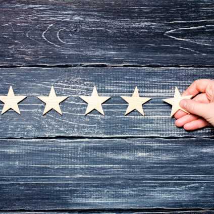A woman's hand puts the fifth star. Quality status is five stars. A new star, achievement, universal recognition. Wooden stars on a black background.
